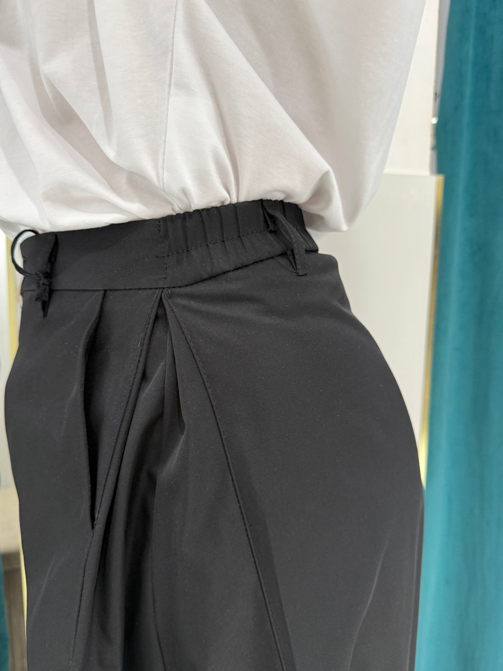 Primo piano ravvicinato del dettaglio della vita del pantalone Justwest, che evidenzia i passanti frontali, la profonda pince laterale e il fascione elastico sul retro.