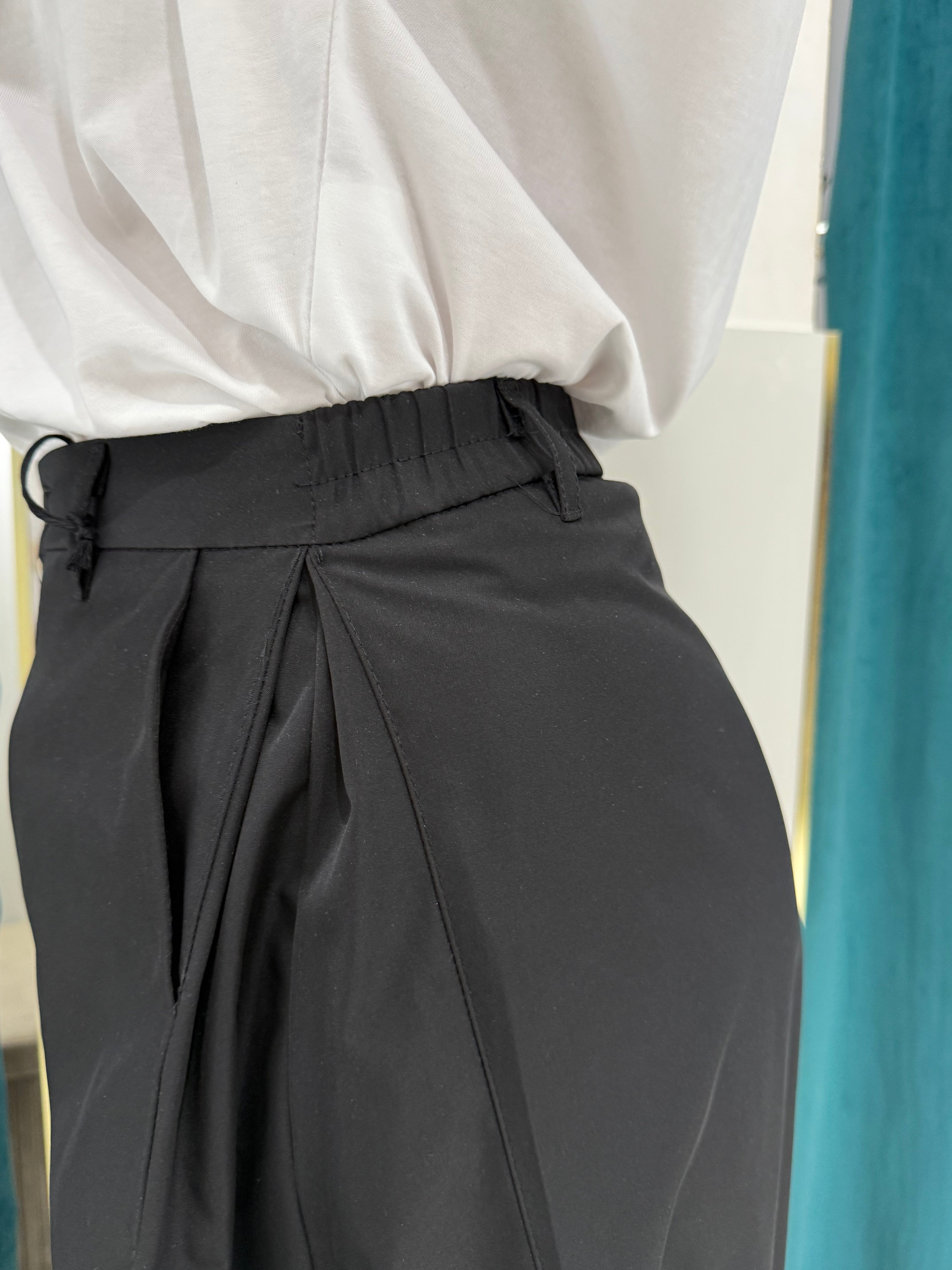 Primo piano ravvicinato del dettaglio della vita del pantalone Justwest, che evidenzia i passanti frontali, la profonda pince laterale e il fascione elastico sul retro.