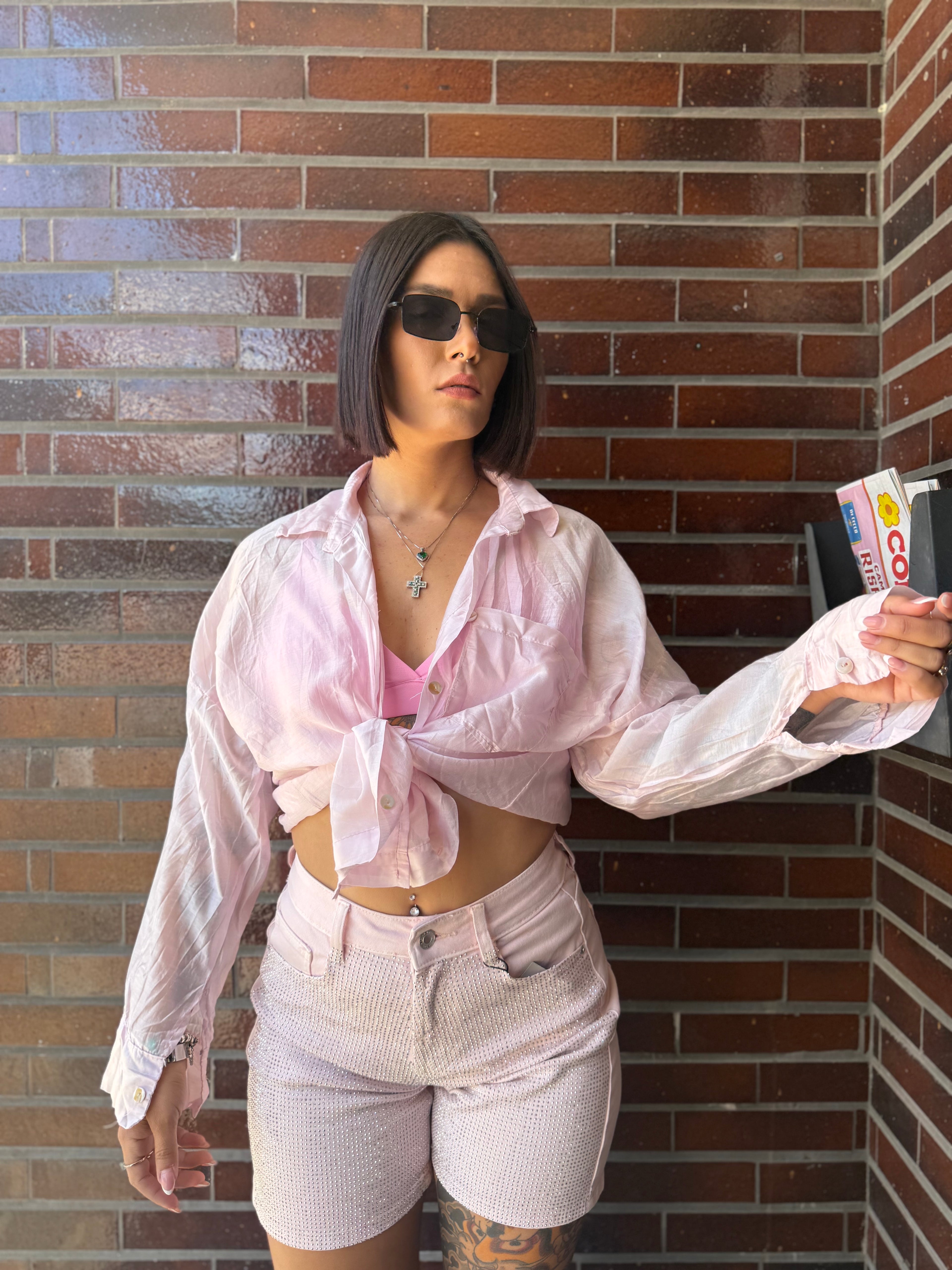 Camicia Velata rosa pastello semitrasparente e mossa FAEV, annodata sul davanti sopra un top a triangolo rosa e jeans con strass.