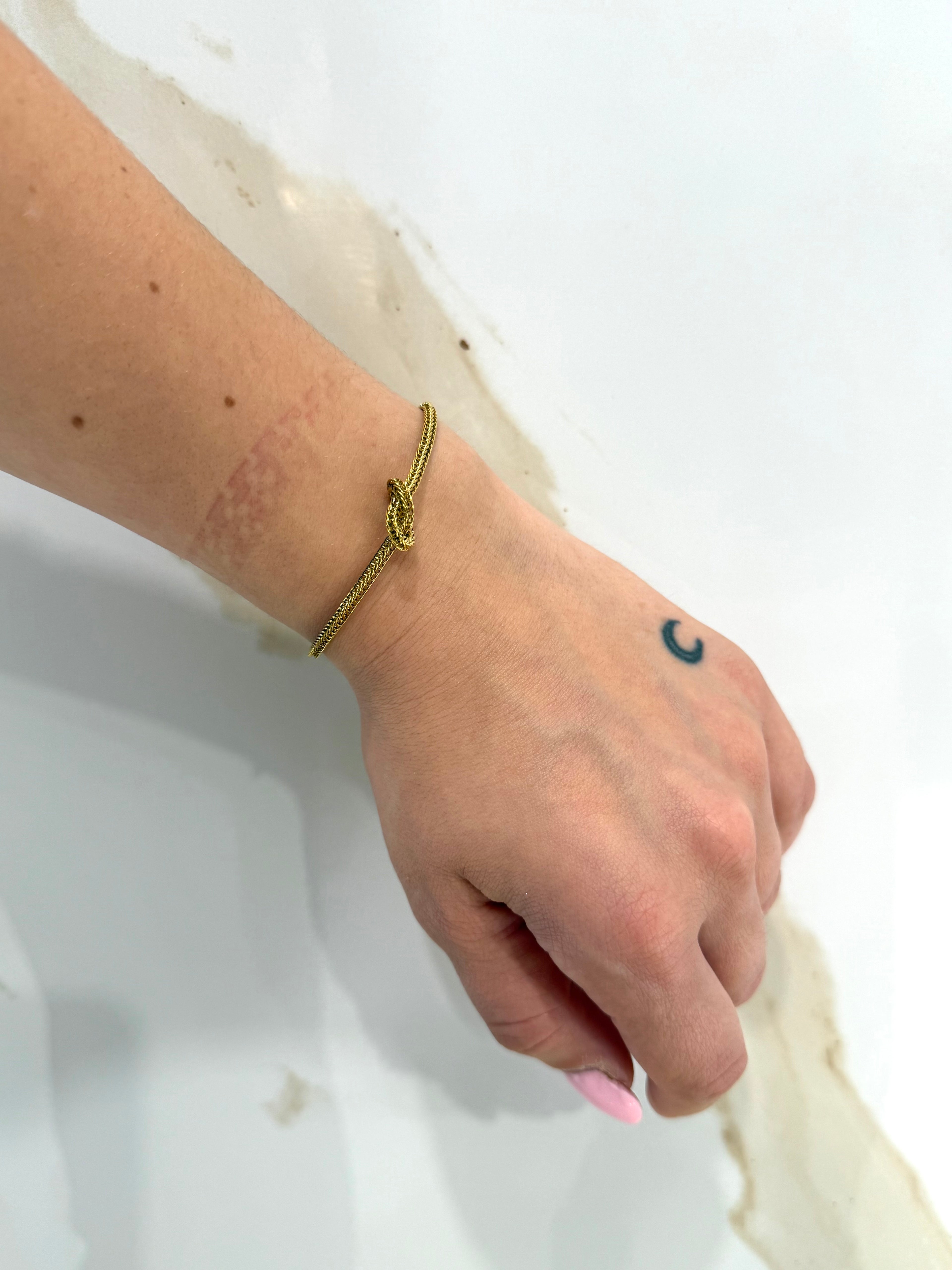 Dettaglio del Bracciale Nodo dorato indossato al polso, che mostra la sottile maglia intrecciata flessibile e il particolare del nodo d'amore al centro.