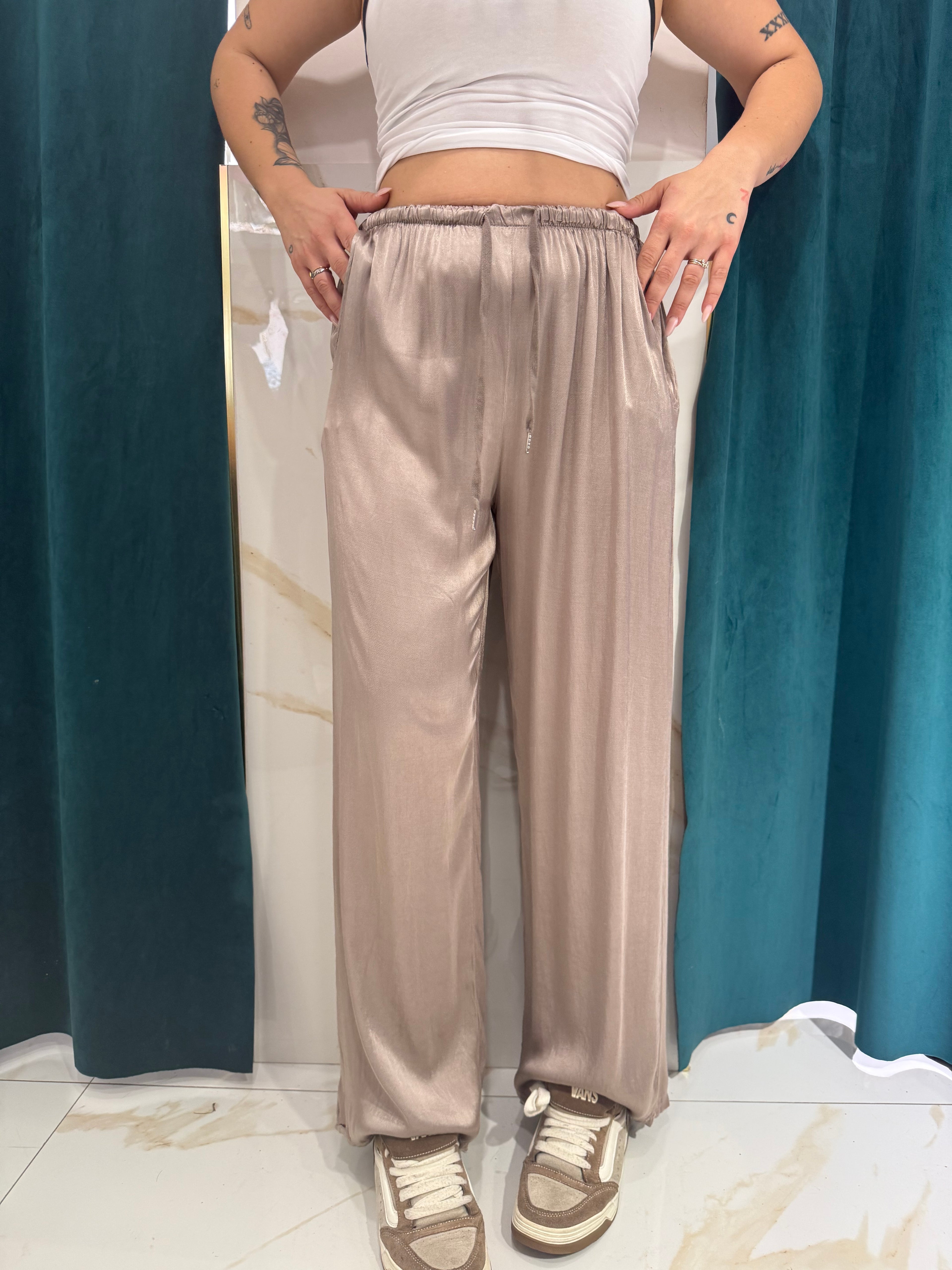 Dettaglio del pantalone a gamba ampia a palazzo in tessuto satinato color tortora lucido indossato con elastico in vita e sneakers marroni