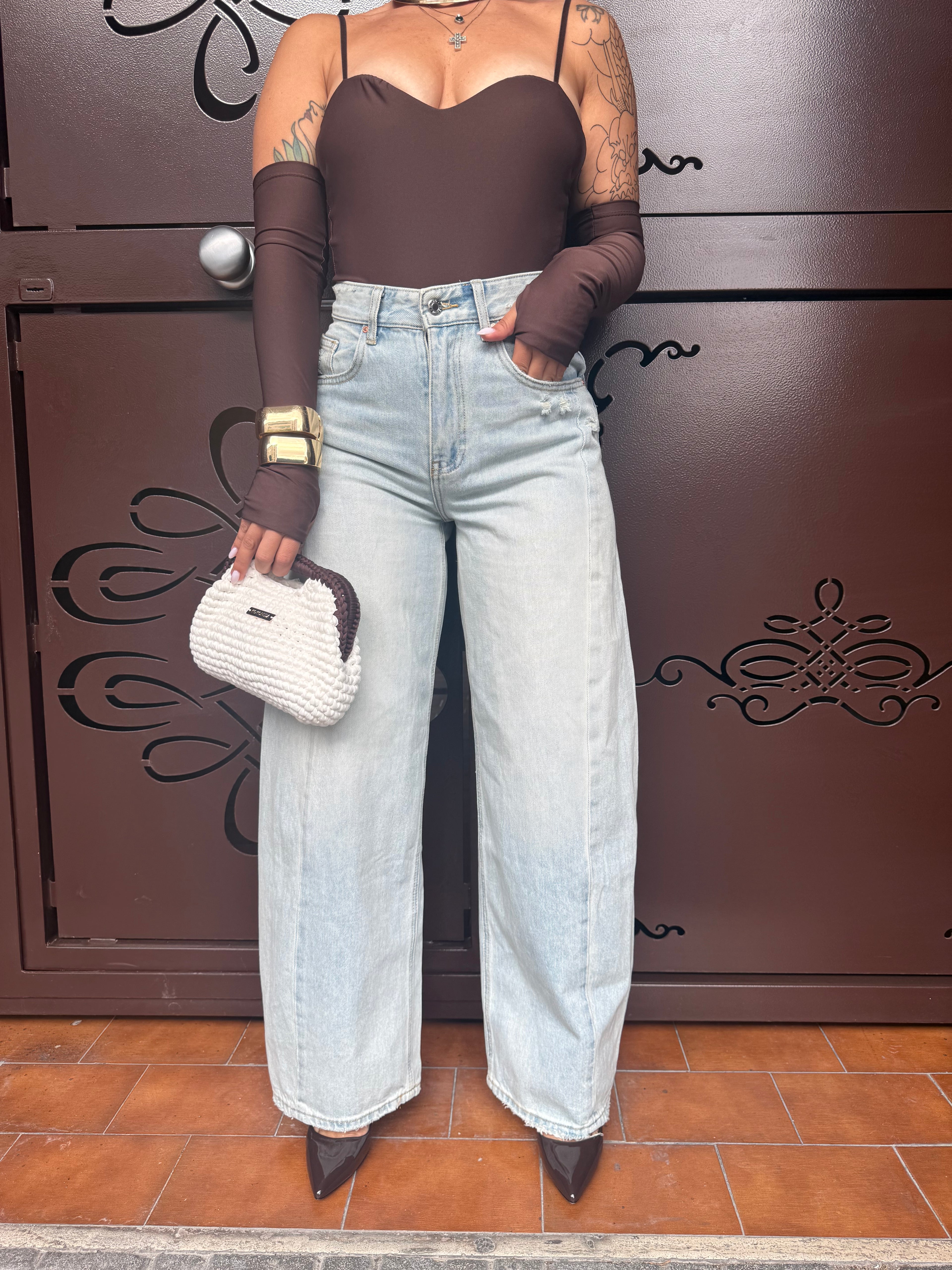 Jeans Malena a gamba larga in denim azzurro chiarissimo con cucitura centrale FAEV, abbinato a body marrone e scarpe a punta.