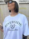 Maxi T-shirt Riverside oversize bianca in cotone con stampa stile college nero FAEV, indossata con occhiali da sole e choker dorato.