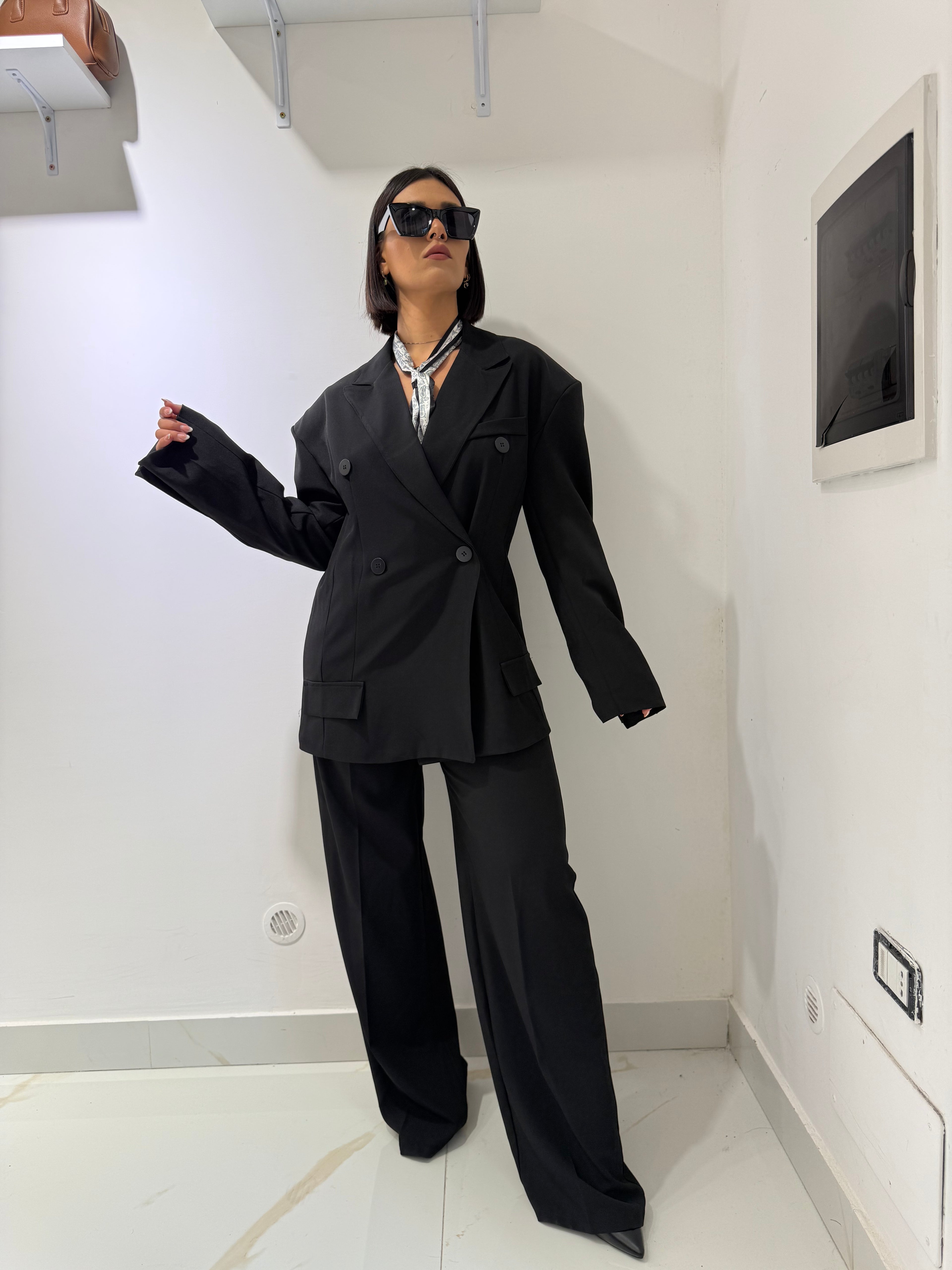Tailleur Wanda due pezzi nero composto da giacca blazer doppiopetto oversize e pantalone a palazzo a gamba larga FAEV, indossato con occhiali da sole.